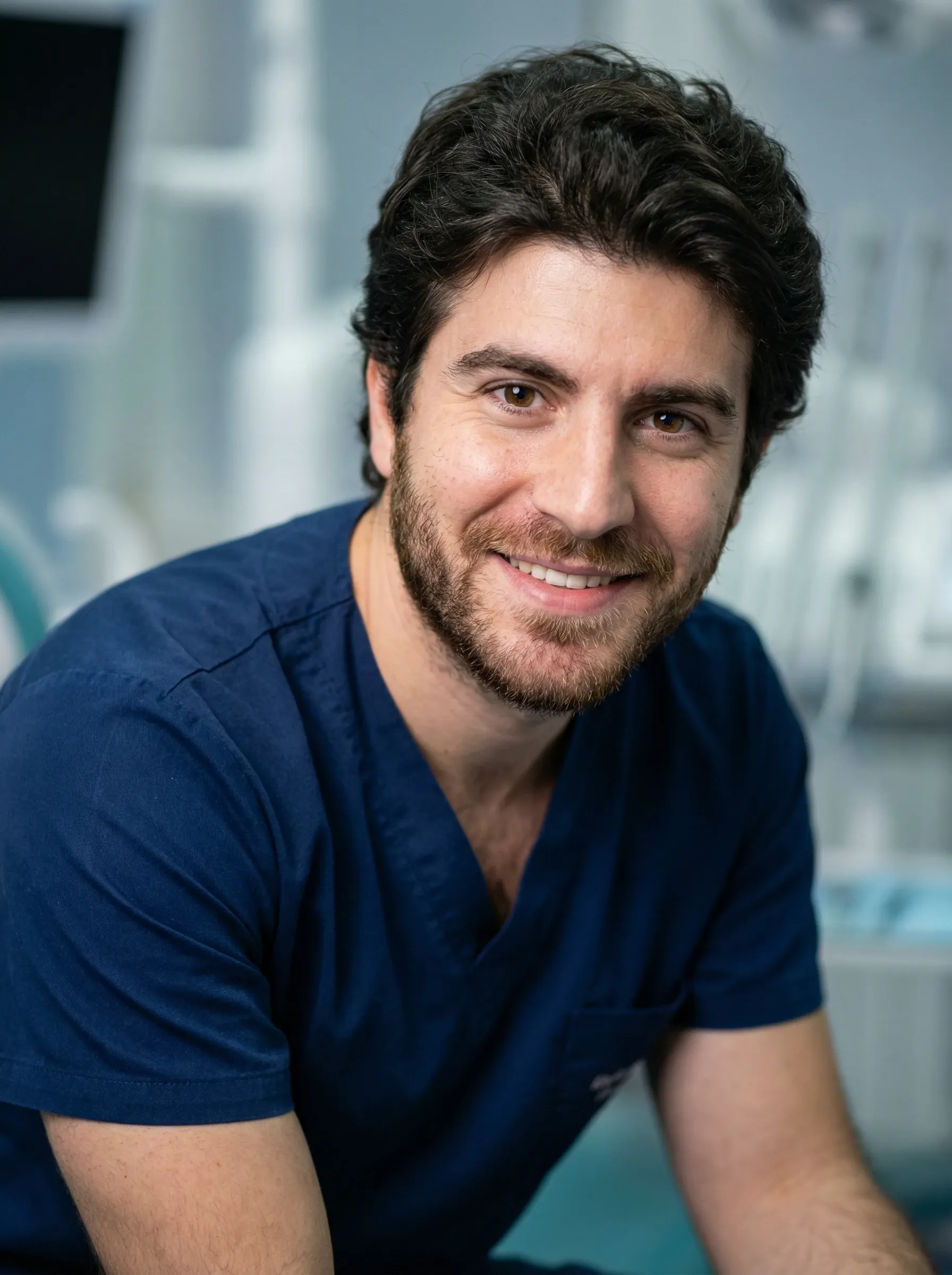 Professional headshot of a man in navy scrubs in a bright clinical setting